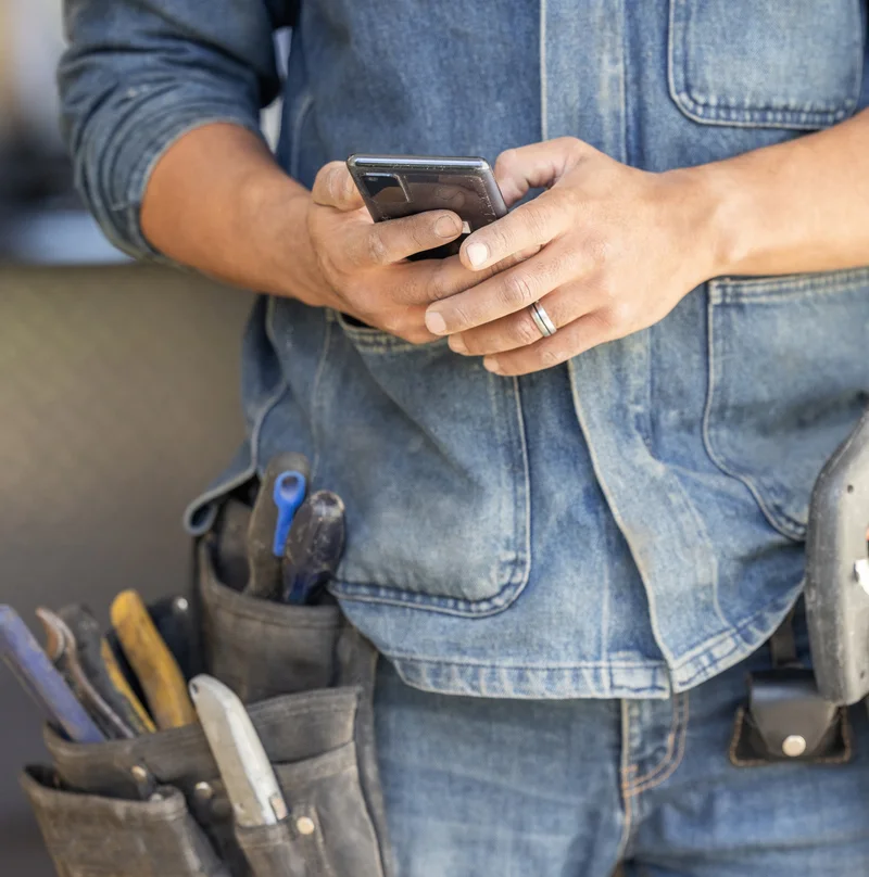 A tradesperson in a tool belt placing an order on their phone